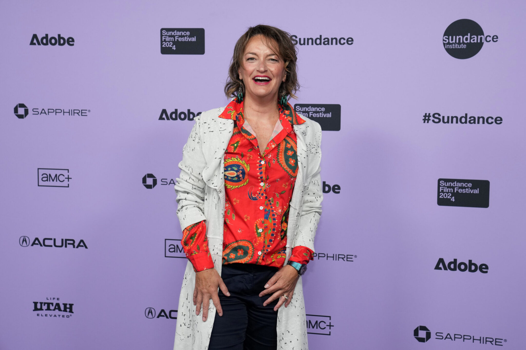 Sally Aitken smiles in front of a white 2024 Sundance Film Festival backdrop.