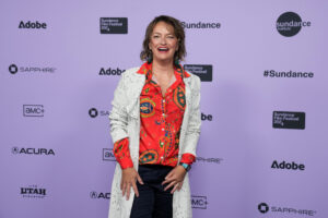 Sally Aitken smiles in front of a white 2024 Sundance Film Festival backdrop.