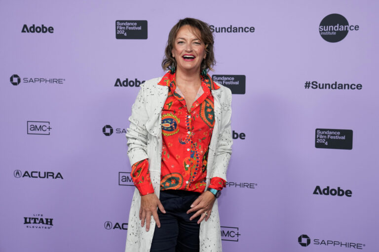 Sally Aitken smiles in front of a white 2024 Sundance Film Festival backdrop.