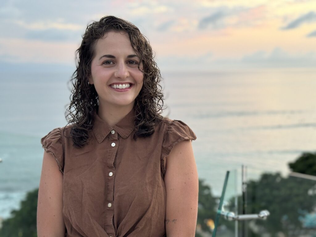 brown curly haired woman smiling in front of the ocean