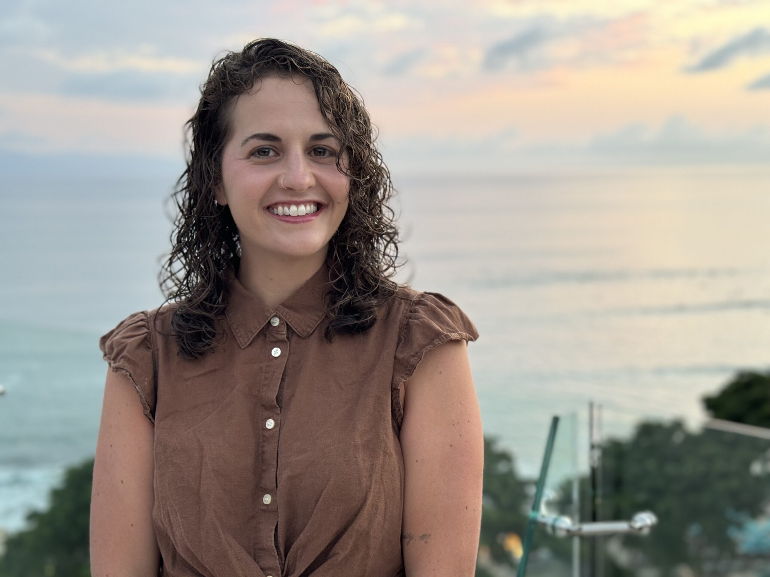 brown curly haired woman smiling in front of the ocean